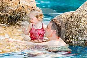 Active father teaching his toddler daughter to swim in pool