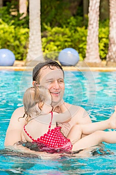 Active father teaching his toddler daughter to swim in pool on tropical reso