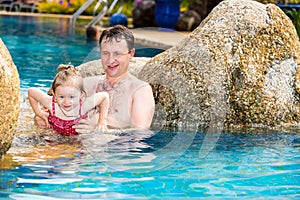 Active father teaching his toddler daughter to swim in pool on tropical resort.