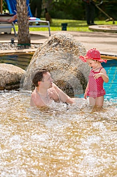 Active father teaching his toddler daughter to swim in pool on tropical resort.