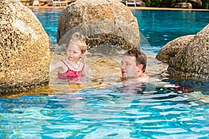 Active father teaching his toddler daughter to swim in pool on tropical resort