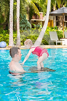 Active father teaching his toddler daughter to swim in pool on tropical resort.