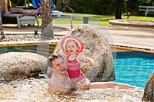 Active father teaching his toddler daughter to swim in pool on tropical resort.