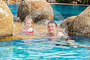 Active father teaching his toddler daughter to swim in pool on tropical resort.