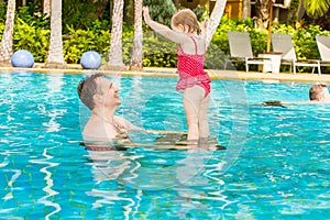 Active father teaching his toddler daughter to swim in pool on tropical resort.