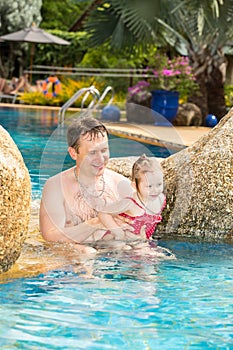 Active father teaching his toddler daughter to swim in pool on tropical resort