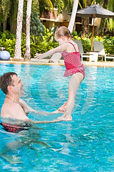 Active father teaching his toddler daughter to swim in pool on tropical resort.