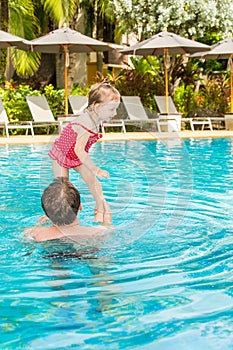 Active father teaching his toddler daughter to swim in pool on tropical resort.