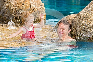 Active father teaching his toddler daughter to swim in pool on tropical resort.