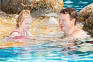 Active father teaching his toddler daughter to swim in pool on tropical resort.