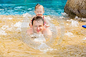 Active father teaching his toddler daughter to swim in pool on tropical resort.