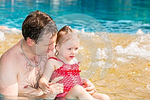 Active father teaching his toddler daughter to swim in pool on tropical resort.