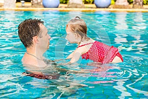 Active father teaching his toddler daughter to swim in pool on tropical resort.