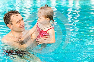 Active father teaching his toddler daughter to swim in pool on tropical resort.