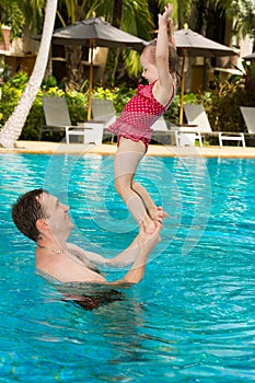 Active father teaching his toddler daughter to swim in pool on tropical resort in Thailand, Phuket.