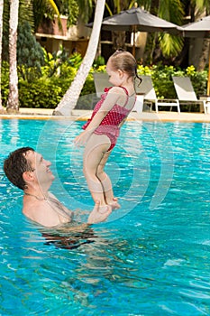 Active father teaching his toddler daughter to swim in pool on tropical resort in Thailand, Phuket.