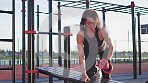 Active female person pumps up forearm muscles using dumbbell