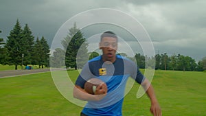 Active fit black American football player with ball passing by defender on field