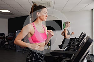 Active fit brunette woman smiling, pink top, running on gym treadmill