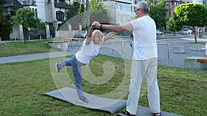 Active fit elderly couple practicing partner yoga while standing on rubber mat.