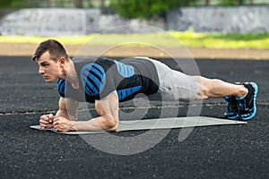 Active fitness man doing planking exercise in the stadium, muscular male workout, outdoors photo