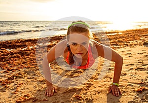 Active fitness woman in sportswear on beach doing pushups