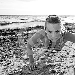 Active fitness woman in sportswear on beach doing pushups