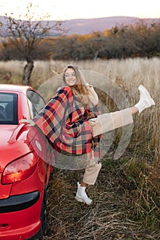 An active girl near a red car in a field outside the city