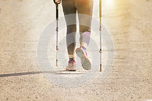 Active girl practicing nordic walking with sticks outdoors against a sun flare. Empty copy space