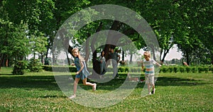 Active girl running around boy on green grass. Playful kids have fun on picnic.