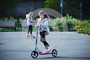 Active girls riding kick scooter and skateboard in skate park. Children having free time playing. The concept of a