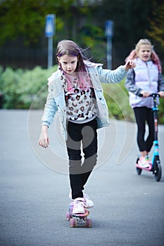 Active girls riding kick scooter and skateboard in skate park. Children having free time playing. The concept of a