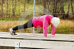 Active grandmum doing push-ups on fresh air.