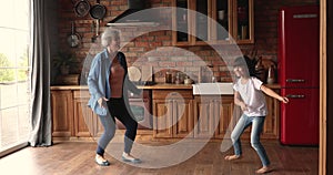 Active granny and granddaughter having fun dancing in kitchen