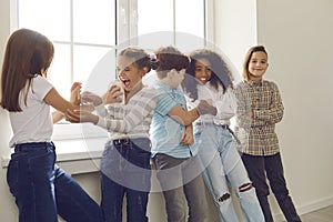 Active group of multiethnic children have fun together and tickle each other standing by the window.