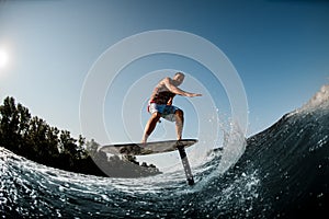 Active guy balancing on the wave with hydrofoil foilboard on background of blue sky