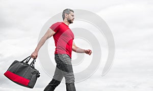 Active guy walking with sporty bag sky background, copy space