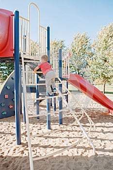 Active happy brave Caucasian boy child climbing staircase climber on playground schoolyard outdoors on summer sunny day. Seasonal