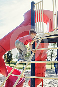 Active happy brave Caucasian boy child climbing staircase climber on playground schoolyard outdoors on summer sunny day. Seasonal