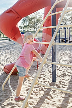 Active happy brave Caucasian girl child climbing staircase climber on playground schoolyard outdoors on summer sunny day. Seasonal