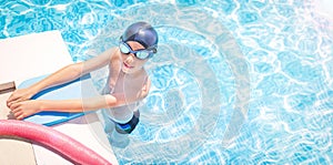 Active, happy child (boy) in cap, sport goggles ready to learns professional swimming with pool board, swim noodles.
