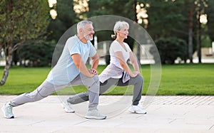 Active happy elderly family couple in sportswear working out together in city park on sunny morning