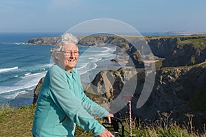 Active happy elderly female pensioner in eighties with mobility frame and walking stick by beautiful coast scene