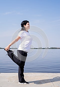 Active and happy senior woman doing stretching near the riverside