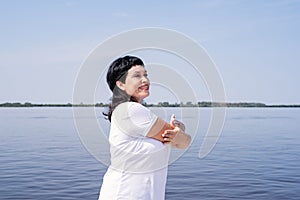 Active and happy senior woman doing stretching near the riverside