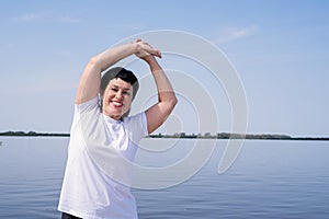 Active and happy senior woman doing stretching near the riverside