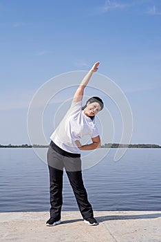 Active and happy senior woman doing stretching near the riverside