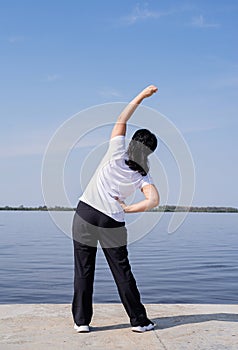 Active and happy senior woman doing stretching near the riverside