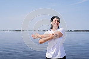 Active and happy senior woman doing stretching near the riverside