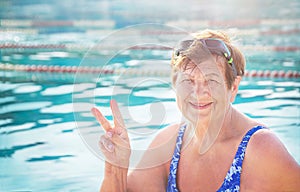 Active, happy senior woman (over age of 50) in swimsuit, sport goggles smiling and doing victory sign.